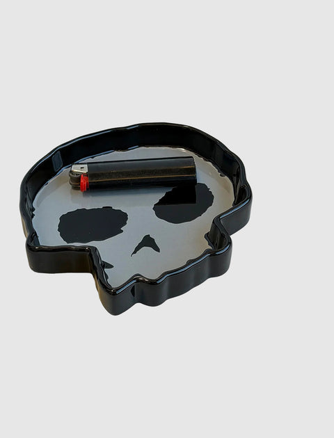 Black skull-shaped ashtray with lighter on gray background
