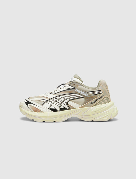 Beige and cream athletic sneaker with black graphic details, side branding, and chunky sole.