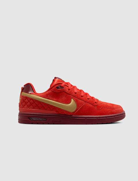 Red low-top suede sneaker with gold Nike swoosh and quilted heel detail on white background