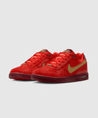 Red and gold low-top sneakers with suede finish, gold swoosh, and maroon sole on grey background