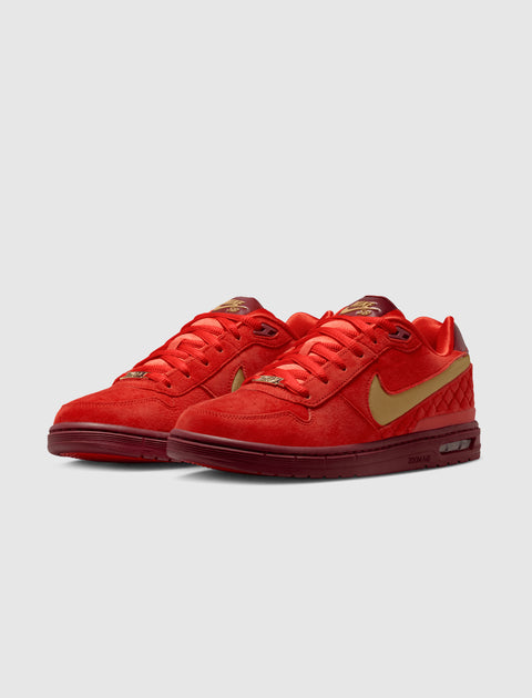 Red and gold low-top sneakers with suede finish, gold swoosh, and maroon sole on grey background