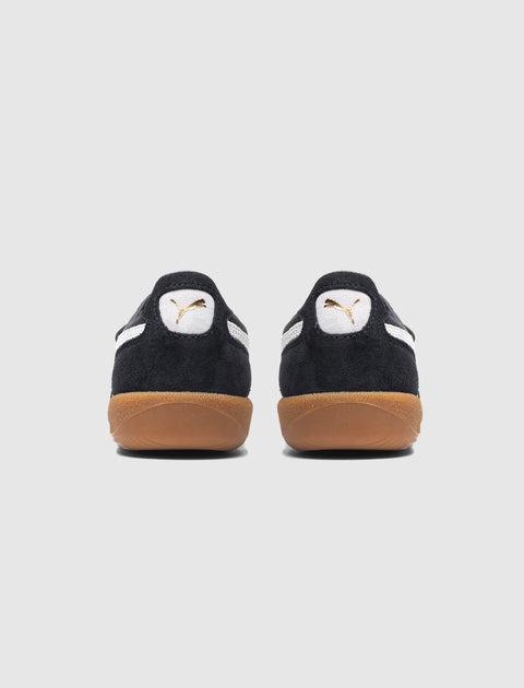 Rear view of black suede sneakers with white logo and gum soles on a light background