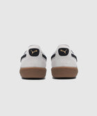 Back view of white suede sneakers with black logo accents and gum soles on white background