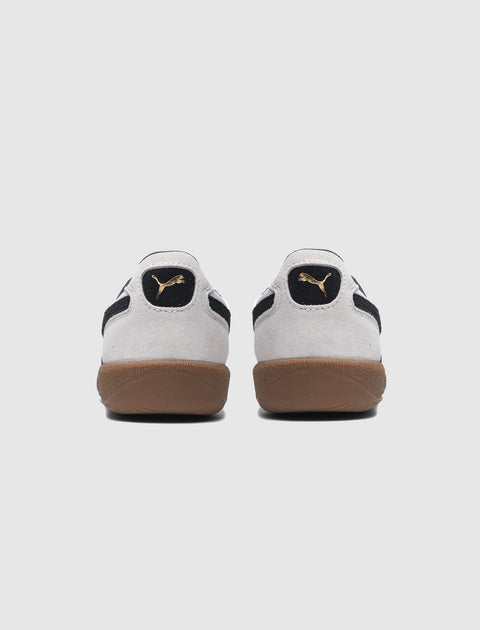 Back view of white suede sneakers with black logo accents and gum soles on white background