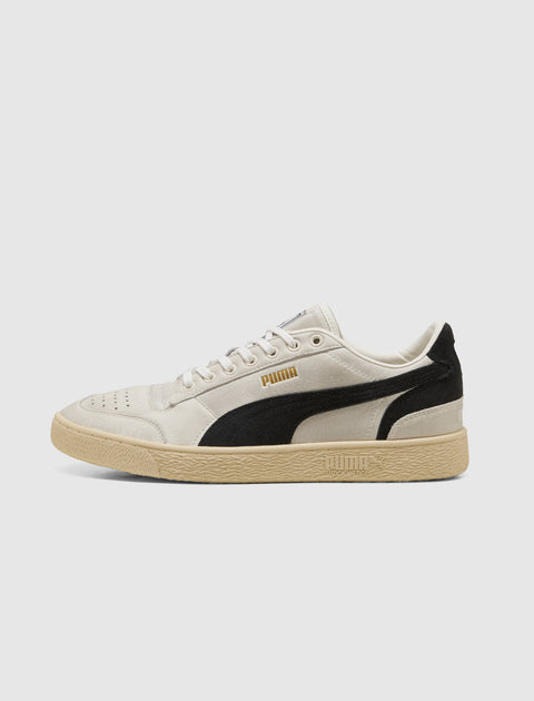 Beige and black low-top men’s sneaker with gum sole, side logo, and suede accents