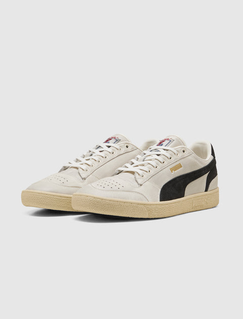 Beige and black low-top sneakers with suede details and rubber soles on white background