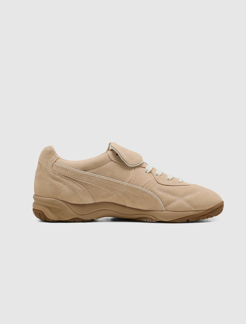 Beige suede sneaker with gum sole, lace-up and velcro strap, side profile on white background