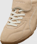 Close-up of beige suede sneaker with white laces and embossed branding on tongue and side
