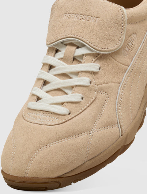 Close-up of beige suede sneaker with white laces and embossed branding on tongue and side