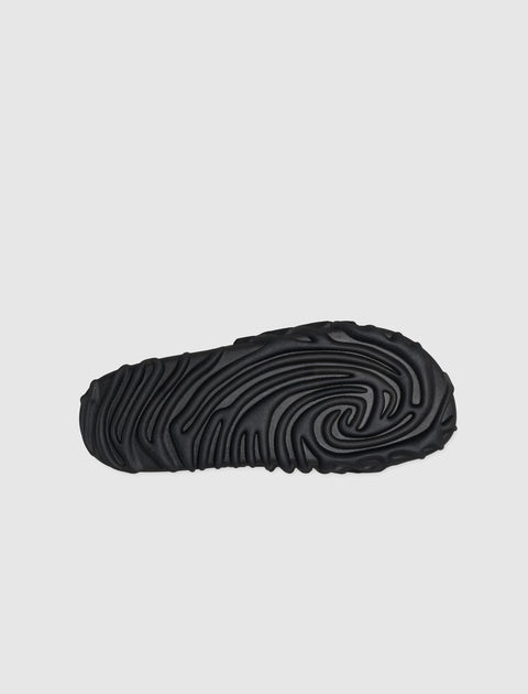 Black slide sandal outsole with textured, wavy tread pattern on white background