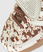 Close-up of a sneaker with brown and white cow print pattern, suede trim, and gum sole