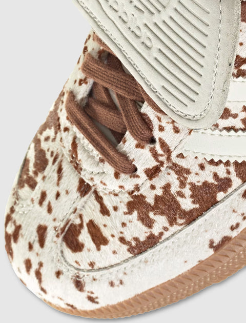 Close-up of a sneaker with brown and white cow print pattern, suede trim, and gum sole