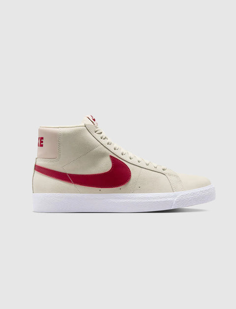 High-top sneaker in pale ivory suede with red swoosh and white sole on a plain background