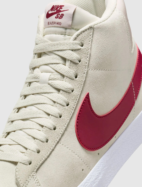 Pale ivory suede mid-top sneaker with red Swoosh logo and white sole, close-up view.