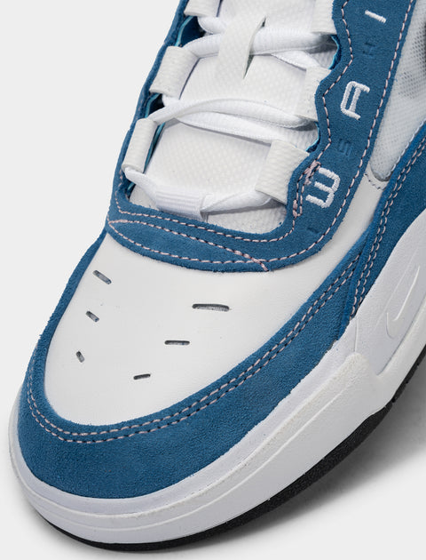 Close-up of a white and blue suede sneaker with white laces and stitched detailing