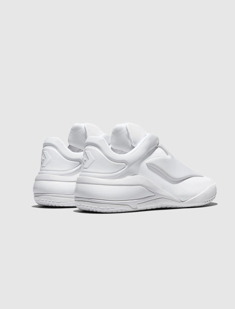 All white low-top sneakers with sculpted sole and textured details, angled rear view