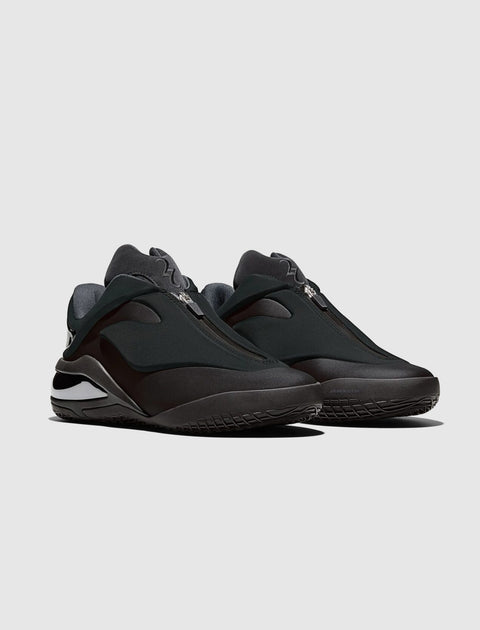Black futuristic low-top sneakers with zip closure and chunky sole on gray background