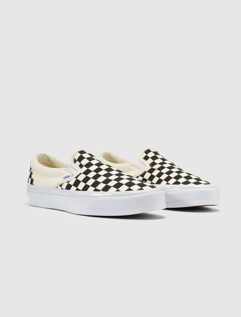 Black and white checkerboard slip-on sneakers with white soles on a plain background