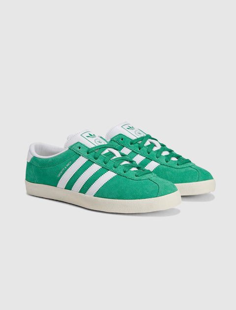 Green suede low-top sneakers with white stripes, white heel tab, and off-white soles