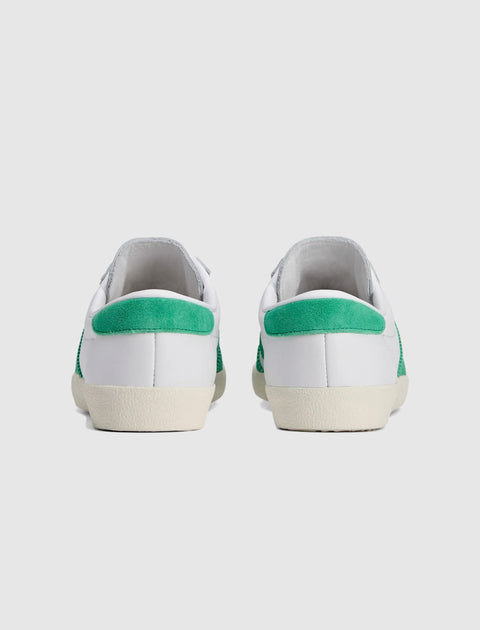 Back view of white sneakers with green suede heel detailing on a plain background