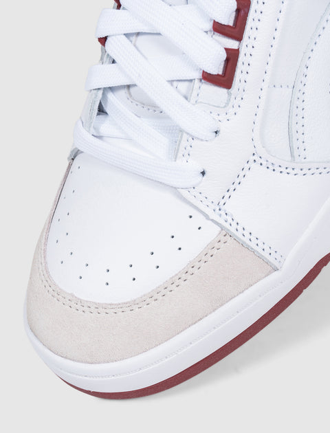 White leather sneaker with beige suede toe, maroon accents, perforated upper, and white laces