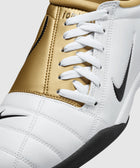 White and gold sneaker with black sole, white laces, and black Nike swoosh logo