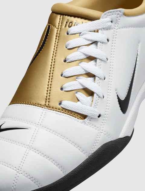 White and gold sneaker with black sole, white laces, and black Nike swoosh logo