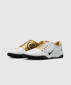 White and gold low-top athletic sneakers with black soles and side logo on a light background