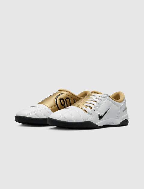 White and gold low-top athletic sneakers with black soles and side logo on a light background