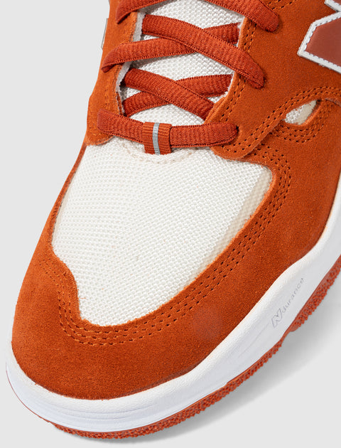 Close-up of orange suede and white mesh sneaker with flat laces and white rubber sole