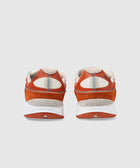 Back view of orange and beige athletic sneakers with white soles on a light background.