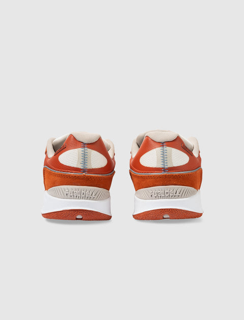 Back view of orange and beige athletic sneakers with white soles on a light background.