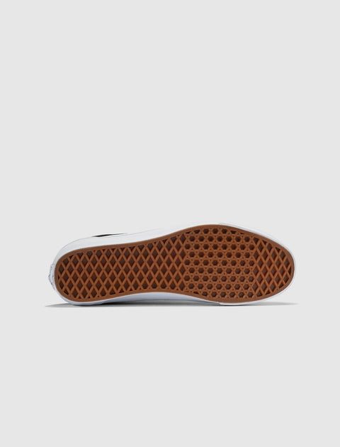 Closeup of black and white sneaker with brown waffle-pattern rubber sole on white background