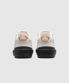 Back view of white and orange low-top sneakers with black soles on a light background.