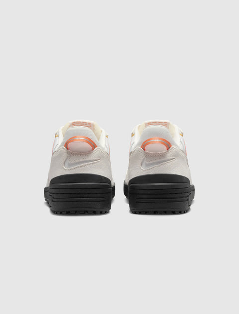 Back view of white and orange low-top sneakers with black soles on a light background.