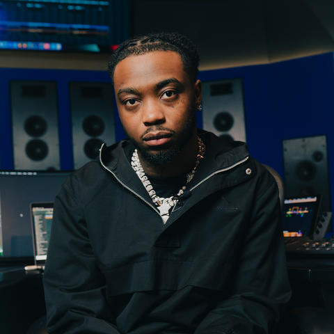 Man in black streetwear jacket with chain necklace sitting in music studio with monitors and speakers
