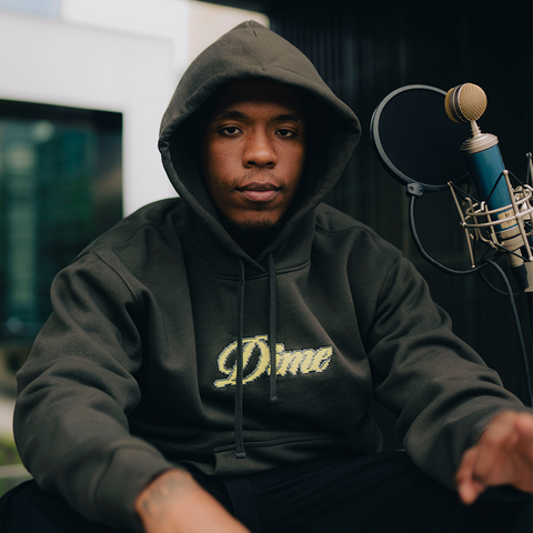 Man in dark green Dime hoodie sitting by microphone, urban streetwear style