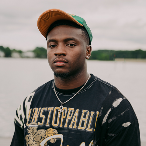 Man wearing black graphic streetwear t-shirt and green cap by water outdoors