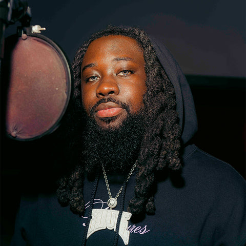 Man with dreadlocks in a black hoodie and pendant necklace recording in a music studio