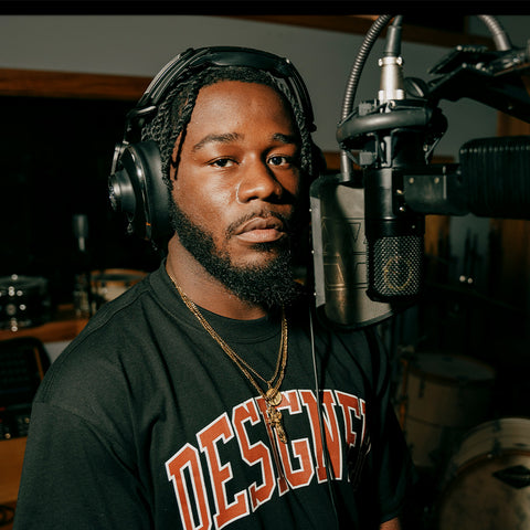 Man in 'Designer' streetwear t-shirt and headphones recording vocals in music studio