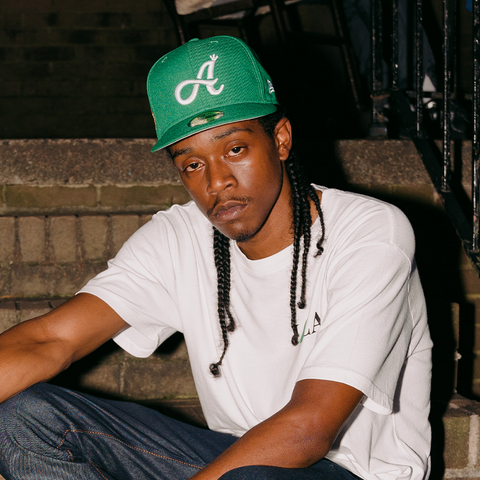 Man in white streetwear t-shirt and green embroidered cap sitting on outdoor steps