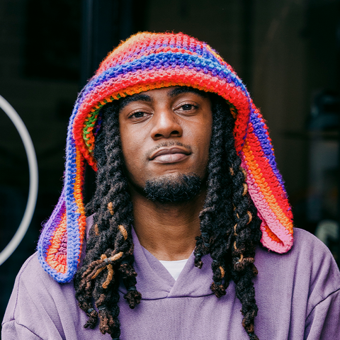 Man in purple hoodie wearing colorful crochet beanie, urban streetwear style
