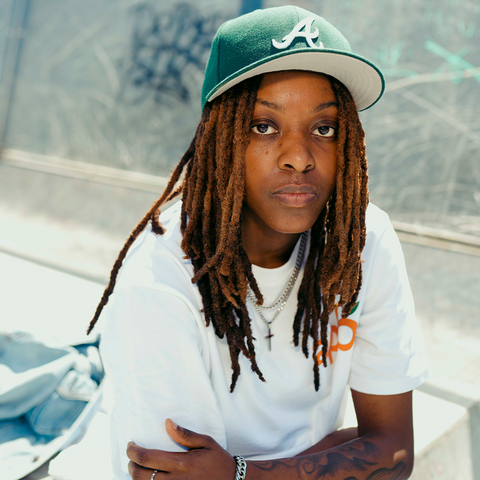 Person in green Atlanta baseball cap, white graphic streetwear t-shirt, and layered necklaces