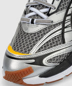 Close-up of a silver and black mesh sneaker with yellow and gum rubber accents