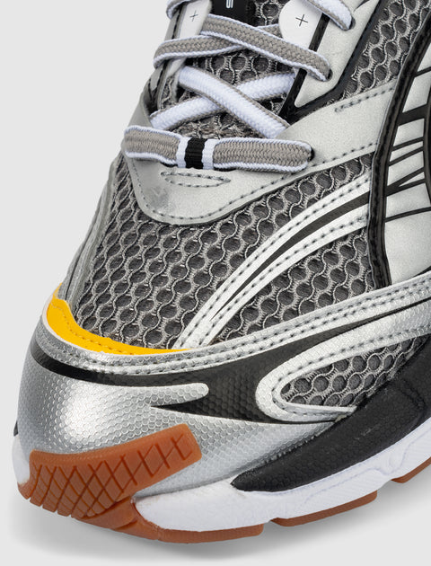 Close-up of a silver and black mesh sneaker with yellow and gum rubber accents