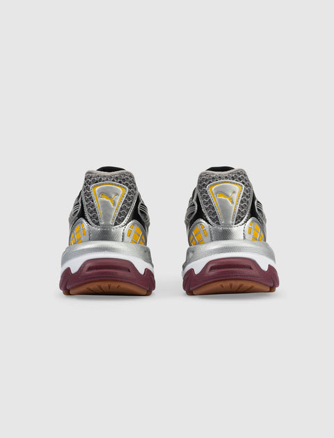 Rear view of metallic silver and yellow sneakers with maroon soles on a white background