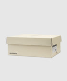 Cream New Balance sneaker box with product label on side, set against a plain background