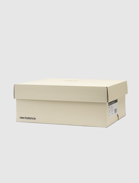 Cream New Balance sneaker box with product label on side, set against a plain background