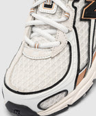 Close-up of white mesh and suede sneaker with black and tan accents, textured sole, and white laces