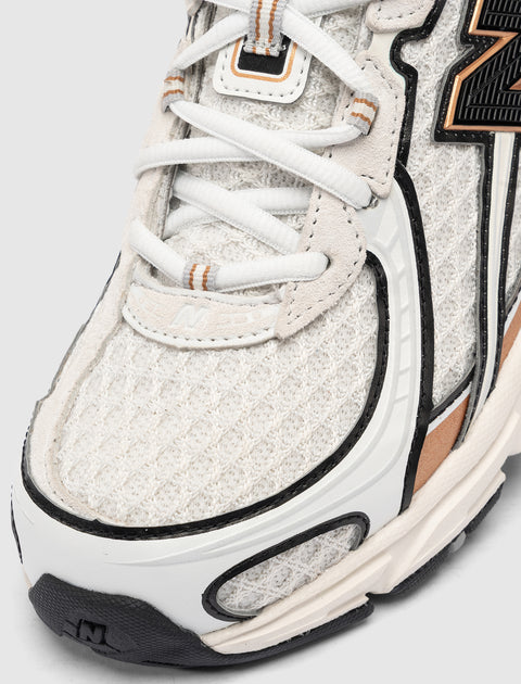 Close-up of white mesh and suede sneaker with black and tan accents, textured sole, and white laces